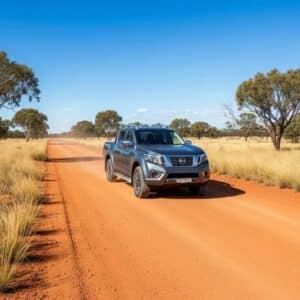 nissan-navara-bush-tile_1 - Midland Cylinder Heads Blue pickup truck driving on a red dirt road through a dry savanna with scattered trees under a clear blue sky.